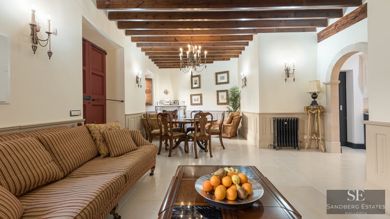 Amplio salón con vigas de madera vista, sofá de rayas y mesa de comedor bajo una lámpara de araña.