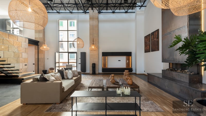Modern living room with double-height ceilings, beige sofas, metal fireplace, and large wicker pendant lights.