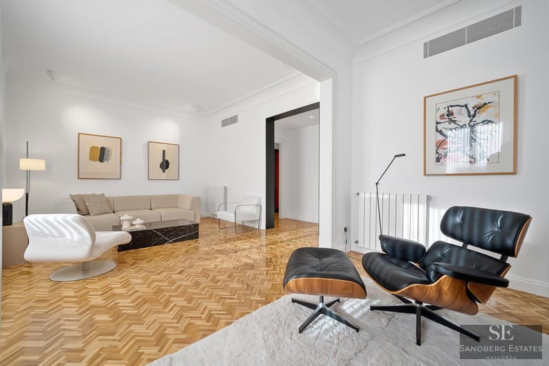 Bright living room featuring a cream sofa, black Eames chair, black marble table, and herringbone wood floors.