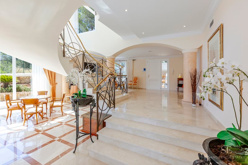 Helle Luxus-Eingangshalle mit weißer Marmortreppe, kunstvollen Eisenreben und Bogenarchitektur.