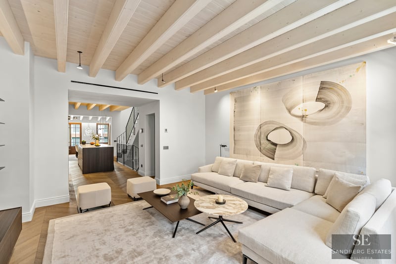 Un salón luminoso con un gran sofá rinconera blanco, vigas de madera en el techo y arte abstracto sobre el sofá.