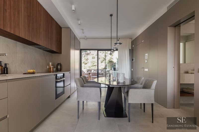 Modern Designer Kitchen and Dining Area Minimalist kitchen with taupe and wood cabinetry, a grey dining table, and large glass doors leading to a terrace.