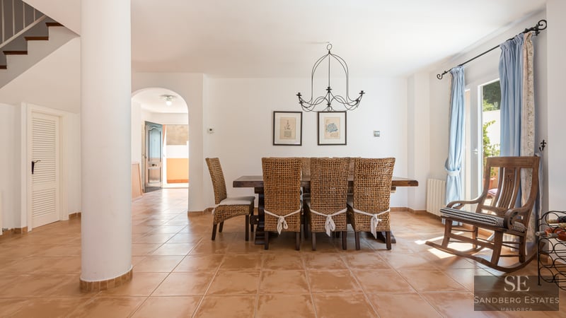 Dining room featuring a large wooden table, wicker chairs, terracotta tile floor, and a wooden rocking chair.
