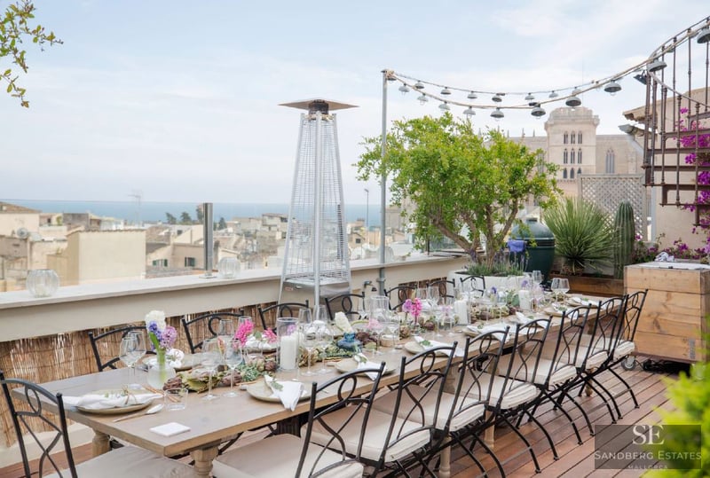 An elegantly set dining table on a wooden deck terrace overlooking a historic city and the sea.