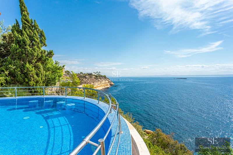 Grand balcon avec vue sur la mer, mobilier moderne, garde-corps en verre. Espace lumineux et élégant. Détails architecturaux design.