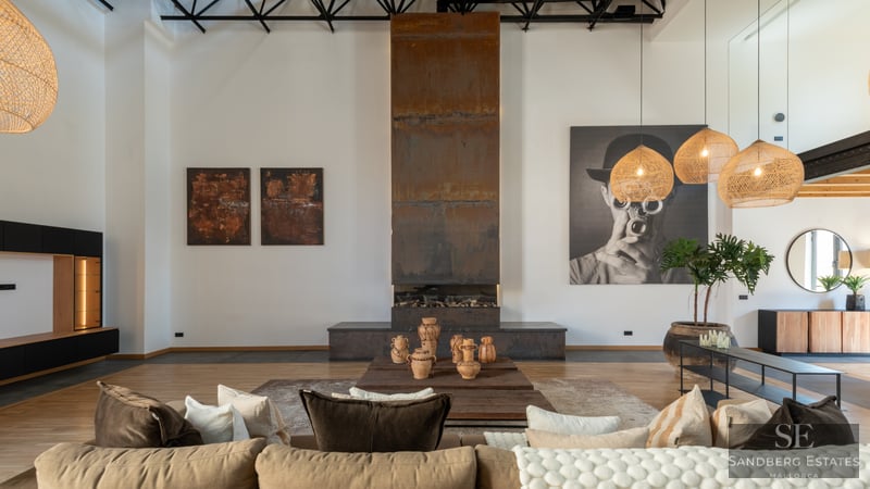 Spacious living room with a tall weathered steel fireplace, beige sofa, and woven pendant lamps in an industrial loft.