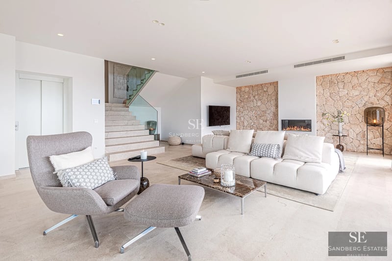 View of an infinity pool with loungers and a lush garden, in front of a modern house with large windows.