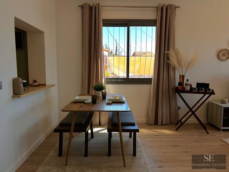 Wooden dining table with benches, neutral curtains, and pampas grass decor by a window.