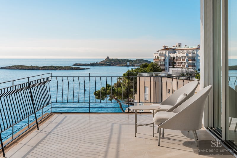 Modern balkong med grå stolar och panoramautsikt över ett blått hav med öar och kustbebyggelse.