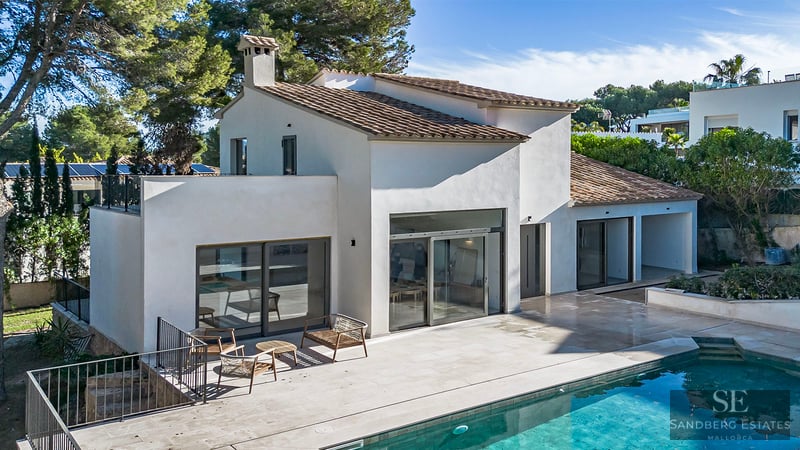 Modern white villa with a terracotta roof, large glass doors, and a stone terrace next to a turquoise swimming pool.