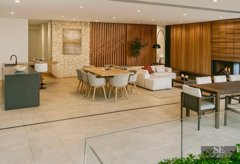 Spacious modern interior featuring a stone accent wall, wooden dining table, white sofa, and a cozy fireplace in the background.