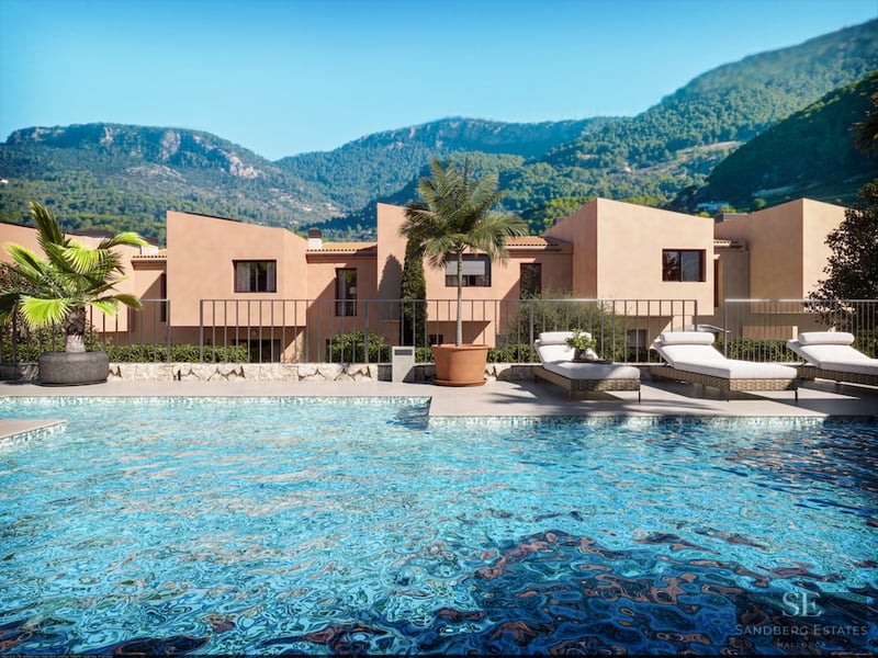 Crystal blue pool with sun loungers in front of terracotta villas and lush green mountains.