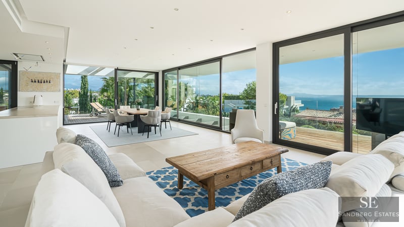 Spacious living room with white sofas, wooden coffee table, and large glass doors opening to a sea-view terrace.