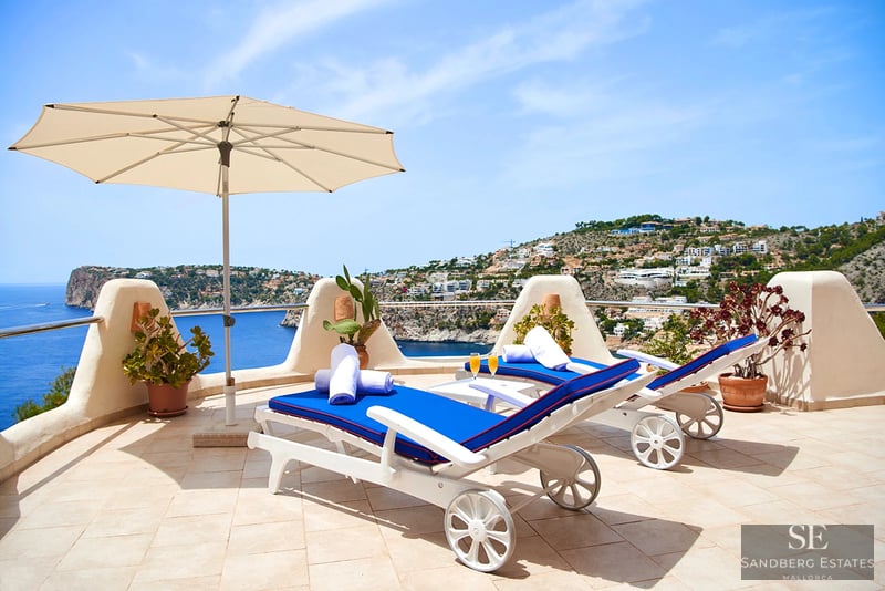 Spacious terrace with pool, sun loungers, and panoramic sea views. Modern design with glass railing and wooden flooring.