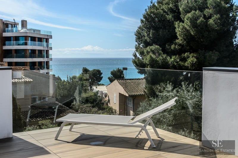 White sun lounger on a modern terrace with a glass railing overlooking the Mediterranean sea.