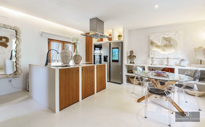 Modern kitchen featuring a wooden island, stainless steel appliances, and a glass dining table with clear acrylic chairs.