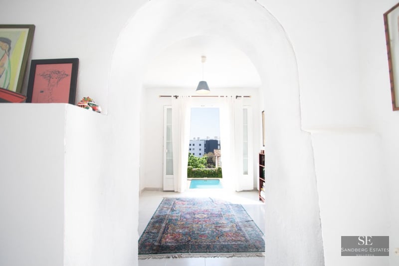A view through a white plastered archway into a bright room with a colorful oriental rug and a pool visible outside.