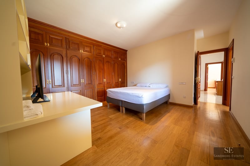 Bright bedroom featuring large built-in wooden closets, hardwood floors, and a minimalist double bed.