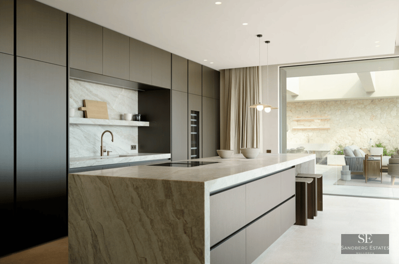 Modern kitchen with large stone island, dark cabinets, copper faucet, and view to an outdoor patio.
