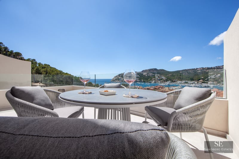 Modern terrace table with two glasses of wine set against a spectacular view of the harbor and sea under a clear blue sky.