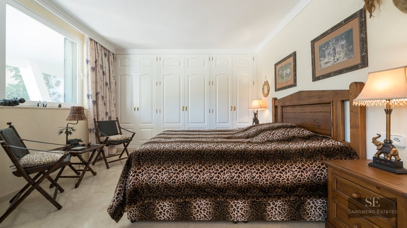 Bedroom featuring leopard print bedding, dark wood furniture, and a full wall of white built-in wardrobes.