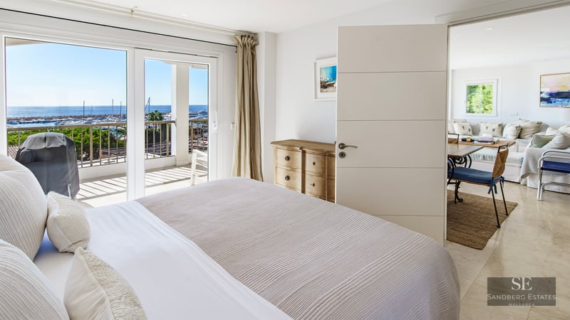 Bright bedroom featuring a large bed, sliding doors to a terrace, and panoramic views of a marina.