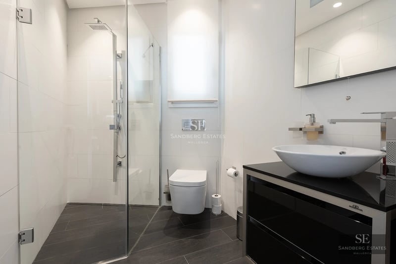Bright modern bathroom with a glass walk-in shower, wall-mounted toilet, and white vessel sink on a black vanity.