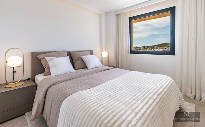 Modern bedroom with a large bed, gold designer lamps, and a window overlooking a city landscape.