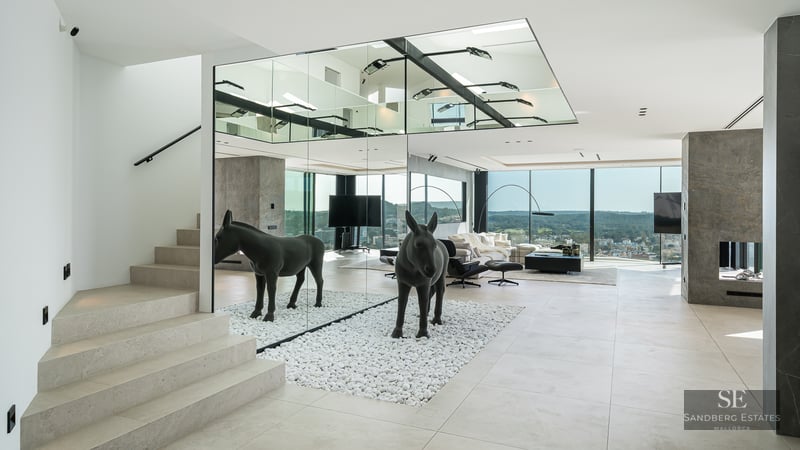 Modern living room featuring a mirrored wall, black donkey sculpture on white pebbles, stone stairs and views.