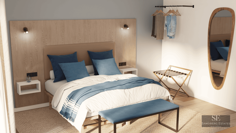 Chambre minimaliste avec tête de lit en bois clair, literie bleue, banc au pied du lit et miroir ovale.