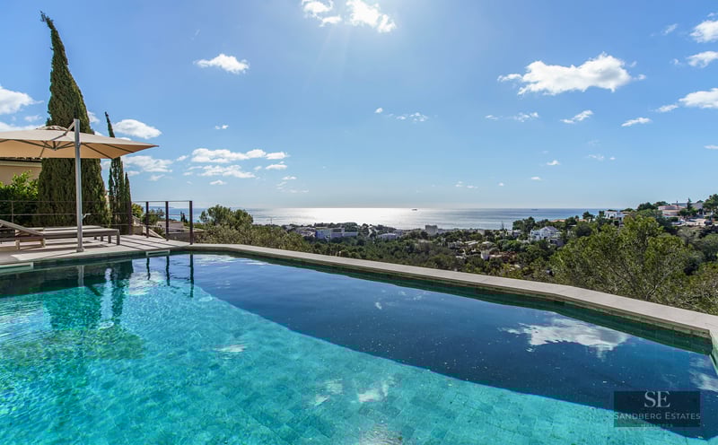 Infinity edge swimming pool overlooking a coastal town and the Mediterranean Sea under a bright sunny sky.