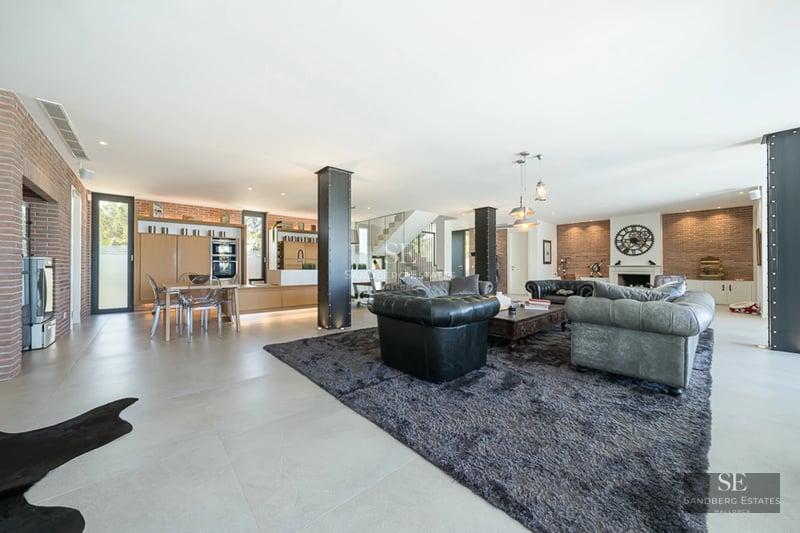 Spacious living room with floor-to-ceiling windows, pool reflecting light, modern design, leather sofas, and elegant coffee table. Natural lighting.