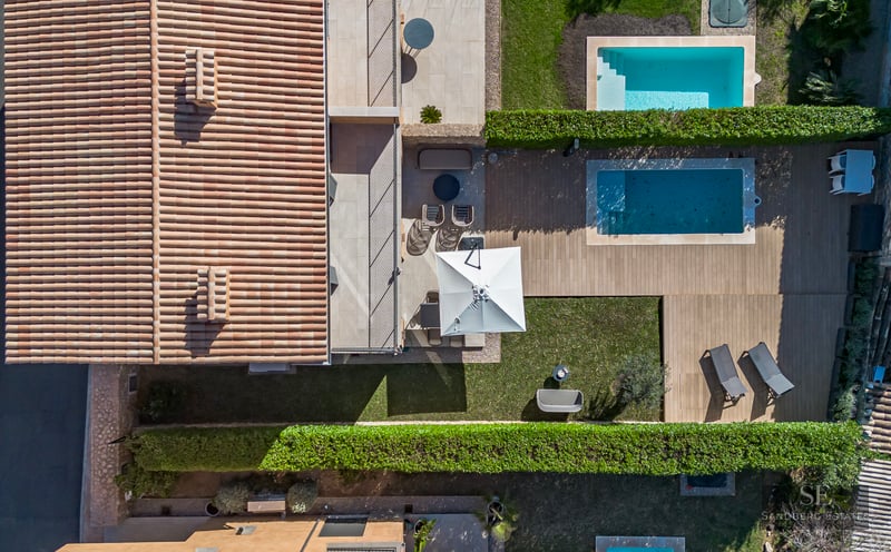 Bird's eye view of a Mediterranean villa featuring a terracotta roof, wooden deck, swimming pool, and lush green lawn.