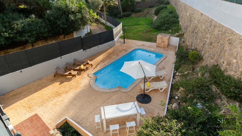 Vue aérienne d'une piscine turquoise entourée d'une terrasse en terre cuite avec transats et coin repas.