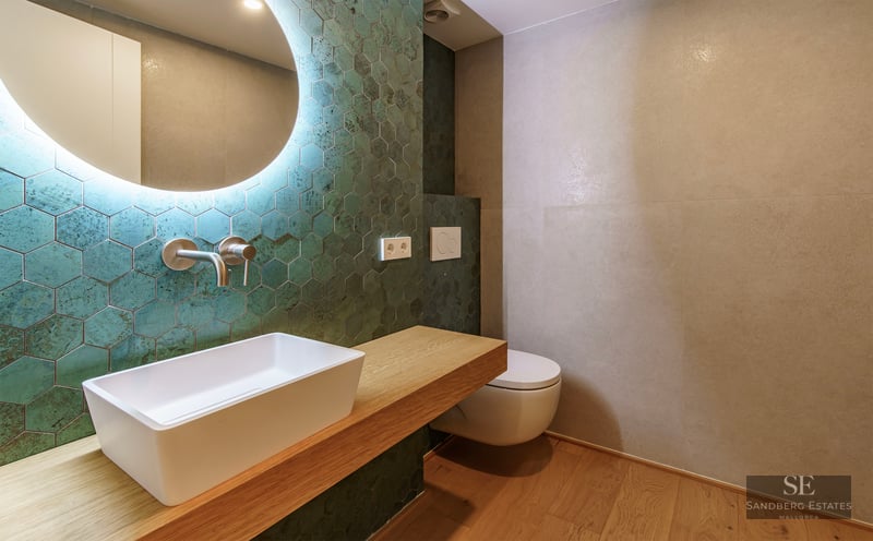 Salle de bain moderne avec carreaux hexagonaux vert canard, vasque à poser sur bois et miroir rétroéclairé.