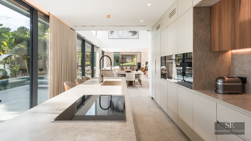 Cuisine moderne avec un grand îlot en pierre, des appareils intégrés et des baies vitrées donnant sur une piscine.