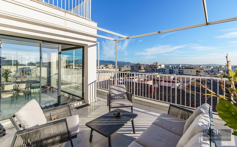 Spacious white terrace with modern outdoor lounge furniture overlooking a cityscape and distant mountains under a blue sky.