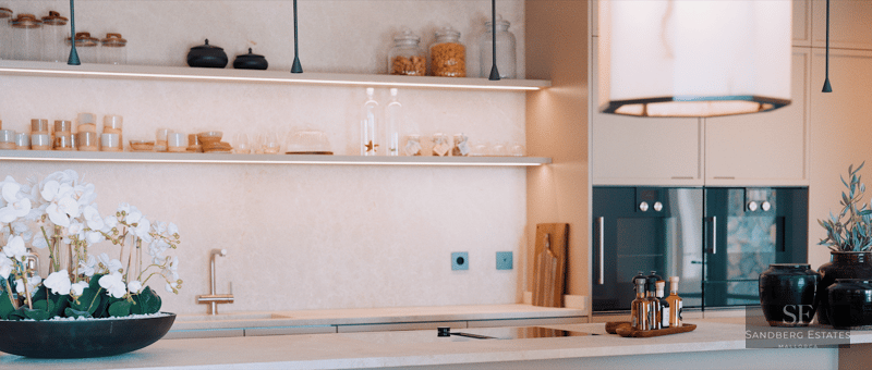 Close-up of a luxury kitchen featuring cream stone countertops, LED-lit open shelving, and integrated appliances.