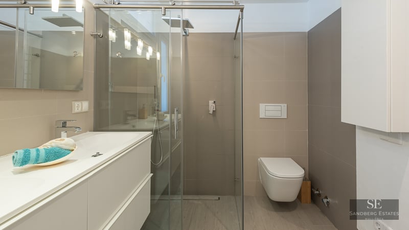 Modern bathroom featuring a white vanity, glass shower enclosure, and a wall-mounted toilet with neutral tiling.