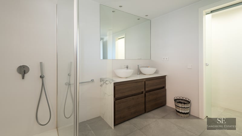 Bright modern bathroom featuring a wood double vanity with marble top, twin vessel sinks, and a glass shower.
