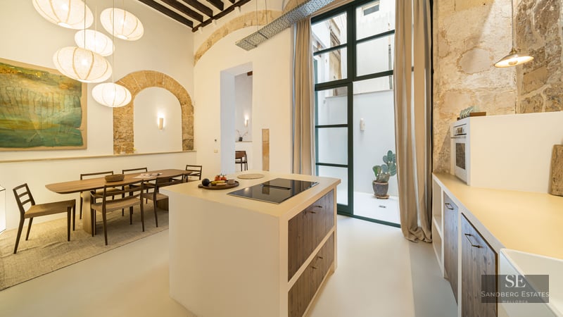 Modern kitchen island, dining area, exposed stone arches, wooden beams, and large paper lantern pendants.