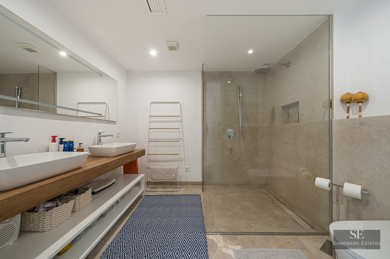 Salle de bain moderne avec double vasque sur plan bois, grande douche vitrée et tapis bleu à motifs.