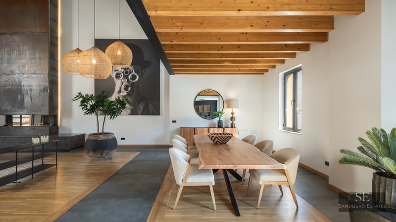 Elegant dining room featuring a live-edge wooden table, upholstered chairs, exposed ceiling beams, and large wall art.