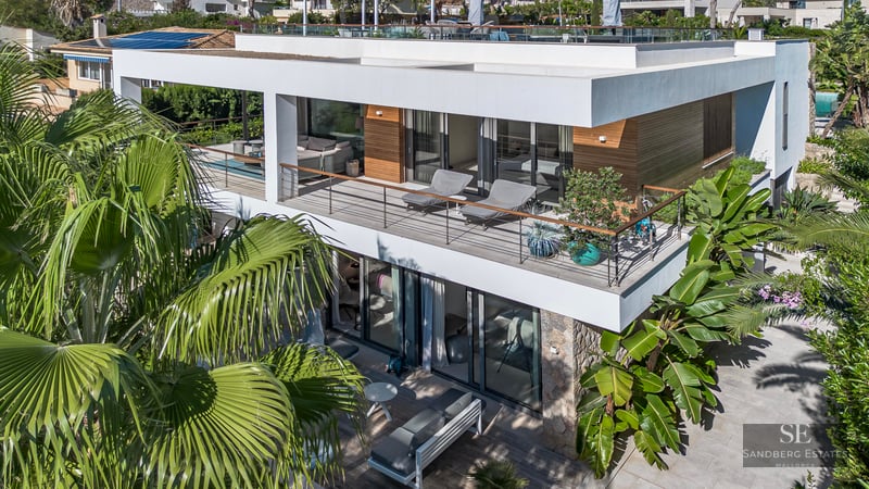 Vue aérienne d'une villa moderne blanche de deux étages avec balcons en verre et palmiers tropicaux.