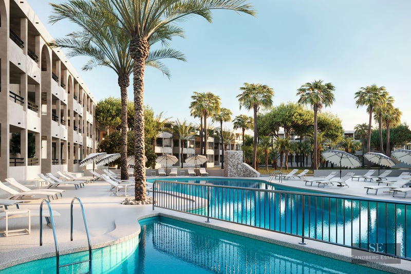 Grande piscine turquoise entourée de chaises longues blanches et de hauts palmiers devant un bâtiment moderne.