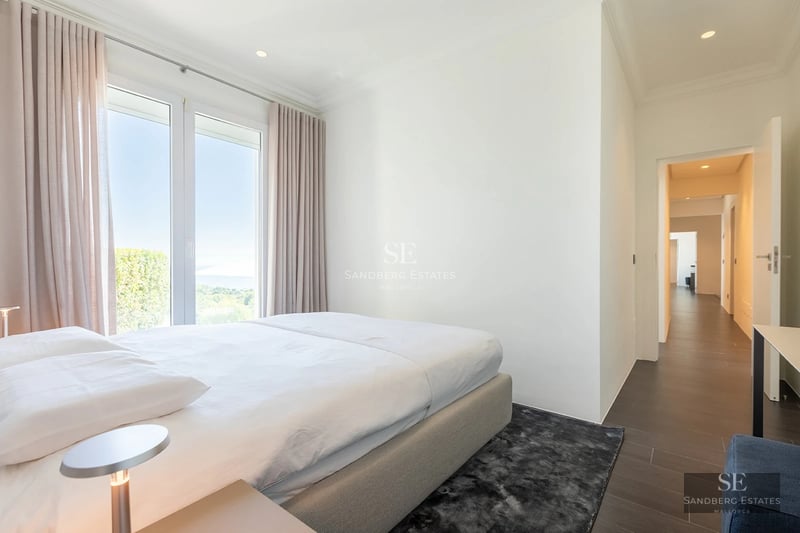 Bright bedroom with a large bed, floor-to-ceiling windows, and elegant neutral-toned curtains.