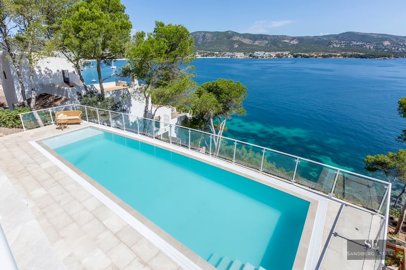 An elevated view of a turquoise infinity pool overlooking the Mediterranean sea with mountains in the background.
