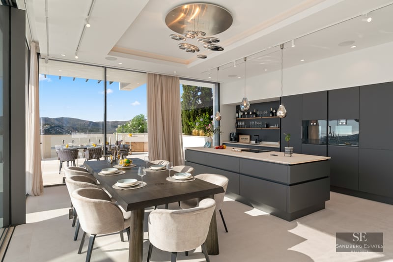 Modern kitchen with large grey island and wooden dining table next to floor-to-ceiling windows with mountain views.