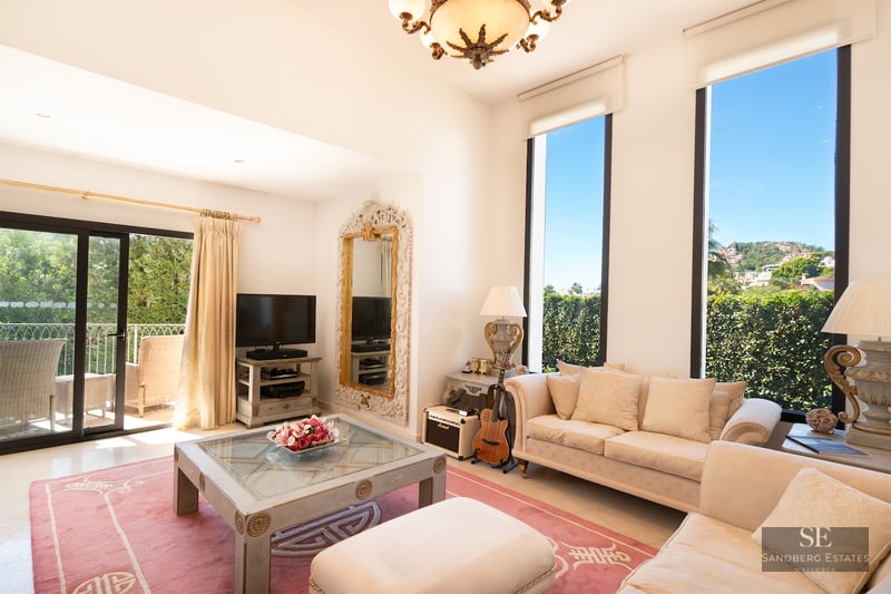Bright living room with cream sofas, a pink rug, large vertical windows, and a sliding door leading to a balcony.