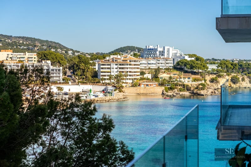 High-angle view of a turquoise bay with white buildings and a marina seen through a glass balcony railing.